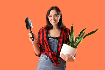 Young woman with plant and shovel on orange background