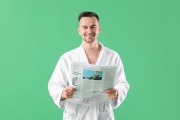 Happy young man in bathrobe with newspaper on green background