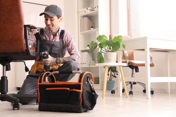Male worker with drill assembling chair in office