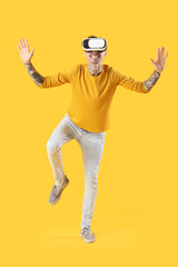 Happy young man in VR headset on yellow background