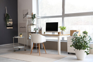 Interior of modern office with workplace, shelf unit and plants