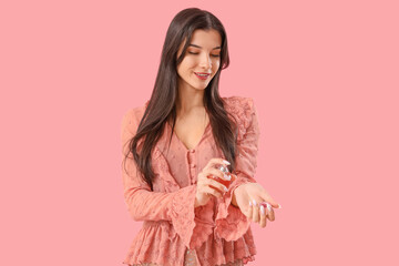 Young woman applying perfume on pink background