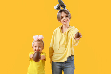 Cute little children in bunny ears with chocolate eggs on yellow background. Easter celebration