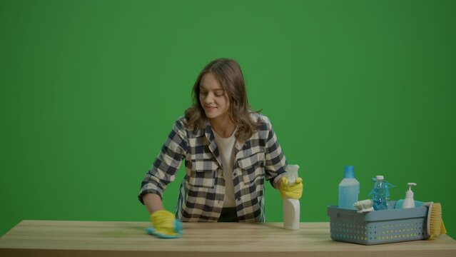Green Screen.A Smiling Young Woman Housewife Cleaning the Table with a Spray Bottle and a Rab,Enjoying Cleaning. Hygiene and Safety Protocols.