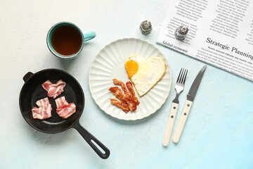 Composition with tasty bacon, fried egg, cup of tea and newspaper on blue background