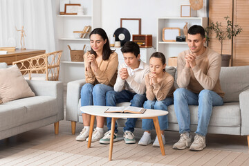 Family praying together on sofa at home - obrazy, fototapety, plakaty