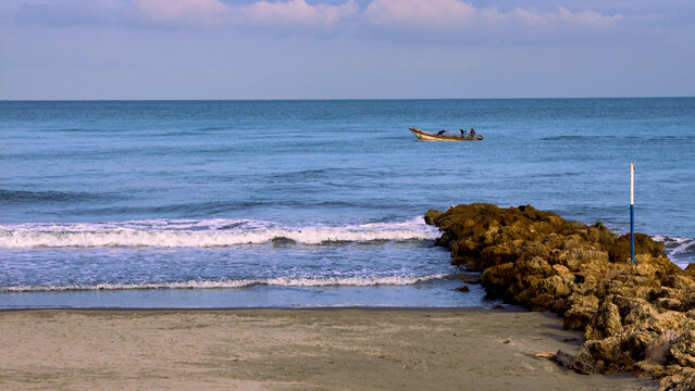 Coastal photo with deep blue sea showing a boat with some unrecognisable fishermen and the beach next to a beach spit in Cartagena, Colombia.