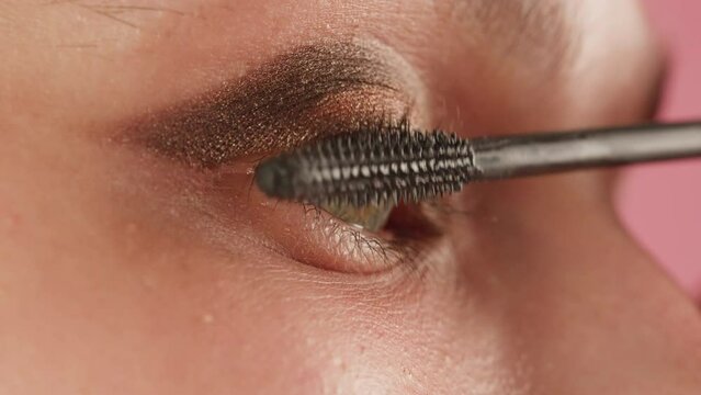 Closeup shot, style artist applies black mascara on the eyelashes of the female eye. Woman making make up using pink mascara. Professional makeup. Making mua. Smoky eyes