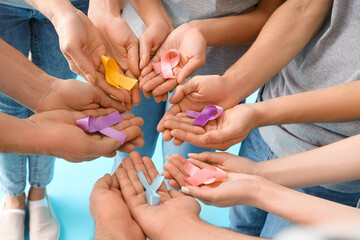 People with different awareness ribbons on blue background, closeup. World Cancer Day