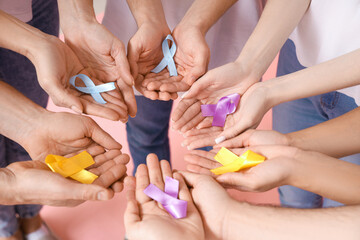 People with different awareness ribbons on pink background, closeup. World Cancer Day