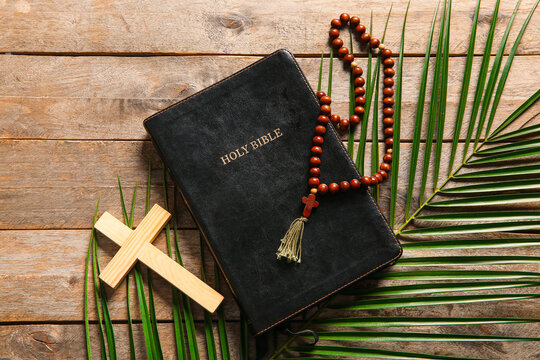 Cross with palm leaves, prayer beads and Holy Bible on wooden background