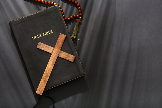 Wooden cross with prayer beads and Holy Bible on black background