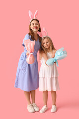 Cute little girl and her mother in bunny ears with Easter gift eggs on pink background