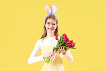 Young woman in bunny ears with tulips on yellow background. Easter celebration