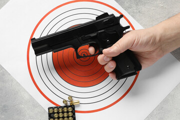 Man with handgun, shooting target and bullets at gray table, top view