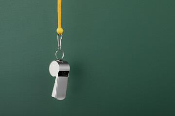 Referee equipment. Metal whistle on dark green background, closeup and space for text