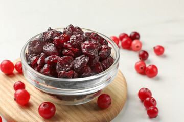 Tasty dried cranberries in bowl and fresh ones on white table, closeup. Space for text