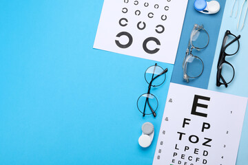 Vision test charts, glasses, lenses and tweezers on light blue background, flat lay. Space for text