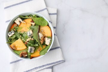 Tasty salad with persimmon, blue cheese and walnuts served on white marble table, top view. Space...