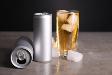 Tasty energy drink with ice cubes in glass and aluminium cans on grey table