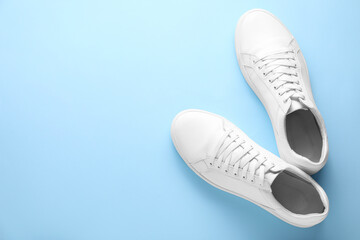 Pair of stylish white sneakers on light blue background, top view. Space for text