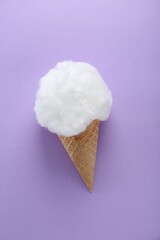 Sweet cotton candy in waffle cone on purple background, top view