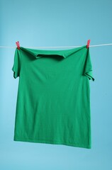 One green t-shirt drying on washing line against light blue background