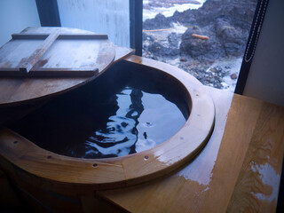 Japanese seaside traditional open air wooden onsen private hot spring bathtub with sliding foggy window and rocky sea shore view