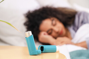 Asthma inhaler on table of sleeping woman in bedroom, closeup