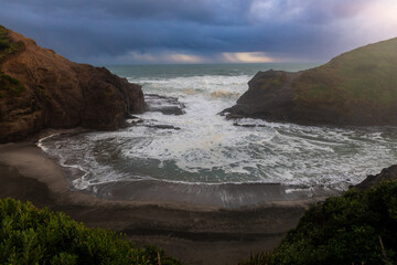 Waves crashing through rocks and onto Sanday shore at sunset. Piha, Auckland, New Zealand.