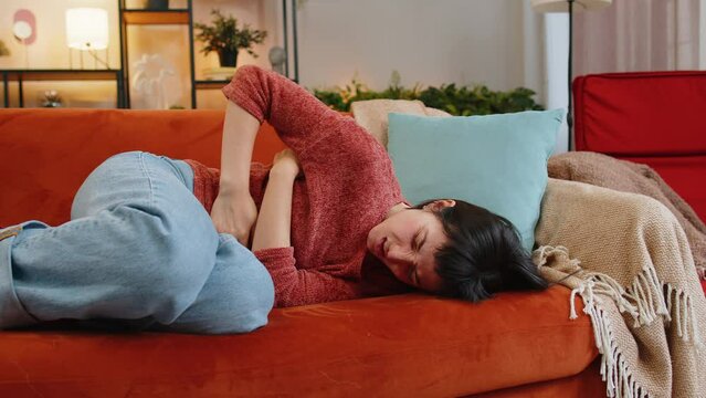 Upset young woman embracing belly suffering from stomachache lying on sofa. Unhappy Caucasian girl having menstrual painful feelings, resting on couch. Gastritis, abdominal or period pain concept