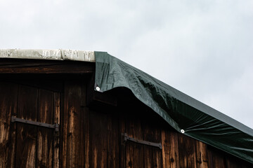Tarp on a rooftop of an old rural building to prevent damage caused by rain water. Keeping a house...