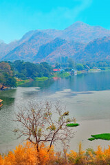 Landscape of a river and mountains with orange-color trees at foreground