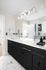 A bathroom with a black cabinet, white marble countertop with two sinks, and a white and black patterned tile floor.