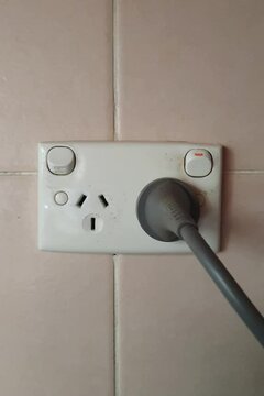 close up of person plugging cord into Australian electrical power point with three pins on tiled wall