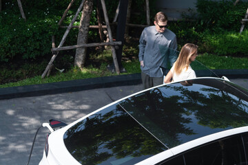 Young couple travel with EV electric car charging in green sustainable city outdoor garden in...