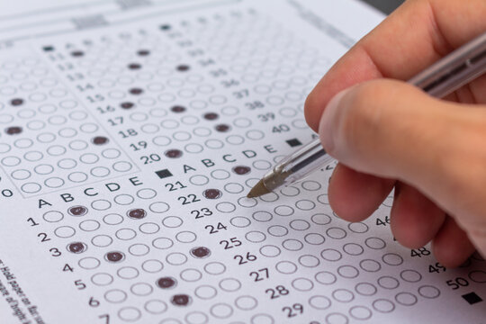 Hand filling out an exam answer sheet with a pen, concept for public and entrance exams.