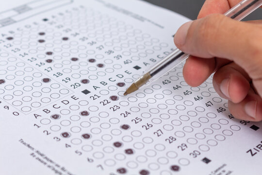 Hand filling out an exam answer sheet with a pen, concept for public and entrance exams.