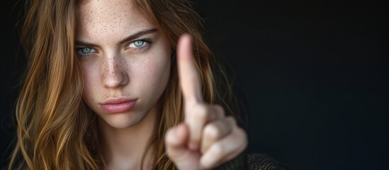 Close-up head shot of a spiteful young lady making an offensive gesture by raising her middle finger.