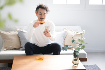 Bearded man drinking coffee in living room with green foreground blur and copy space