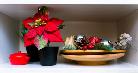 Christmas Shelf Decor with Poinsettia and Ornaments. A cozy shelf arrangement featuring a vibrant poinsettia plant, pinecones, red and gold baubles, and a small decorative red pot