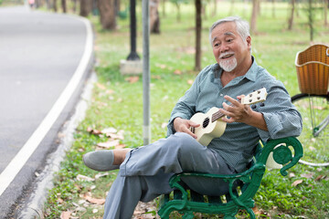 Obraz premium senior man playing ukulele and looking forward in a park