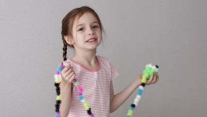 A little girl shows a long snake made from a sticky bunchems constructor, smiling and looking into the frame.