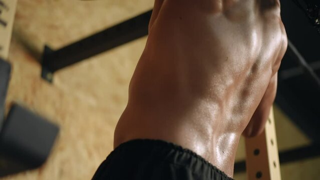 Close-up. An athletic man of mixed race with dreadlocks on his head is doing pull-ups on the horizontal bar in the gym with his back to the camera