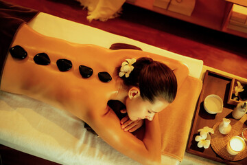 Hot stone massage at spa salon in luxury resort with warm candle light, blissful woman customer...