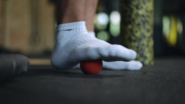 Close-up. A man's socked foot rolls a small hard ball under his foot. Rolling a ball with your feet relieve midfoot discomfort