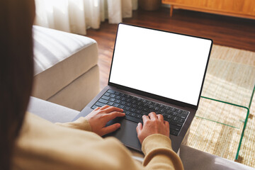 Mockup image of a woman working and typing on laptop computer with blank screen while sitting on sofa at home - obrazy, fototapety, plakaty