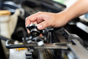 A person is holding a funnel and pouring coolant into the radiator of a car and they are standing in front of a car.