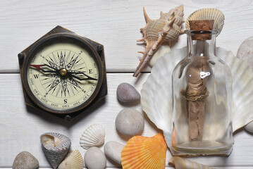 Message scroll letter in the bottle and compass on the white wooden desk table flat lay background.