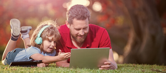 Banner of father on son school boy with laptop study online lying on grass, family blog. childhood and parenthood. happy boy listen music in headphones.